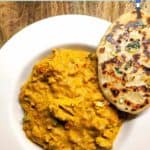 A white bowl of chicken tikka masala with a garlic naan