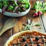 A pissaladiere tart and a bowl of salad on a wooden table
