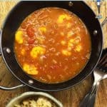 A bowl of prawn curry and a bowl of rice on a wooden table