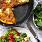 A pan containing frittata on a table with a bowl of salad