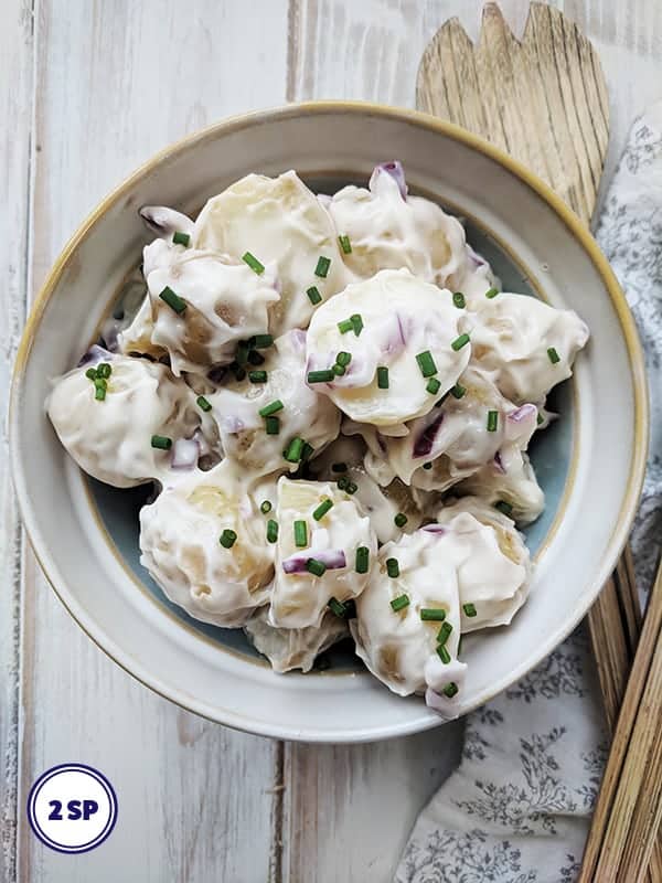 A white bowl of potato salad topped with chopped chives