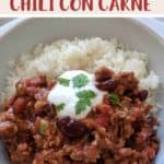 A white bowl filled with chili con carne & rice topped with yogurt and green herbs