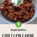 A white bowl filled with chili con carne & rice topped with yogurt and green herbs