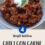 A white bowl filled with chili con carne & rice topped with yogurt and green herbs