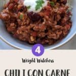 A white bowl filled with chili con carne & rice topped with yogurt and green herbs