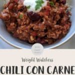 A white bowl filled with chili con carne & rice topped with yogurt and green herbs