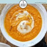 A bowl of carrot & lentil soup on a wooden board