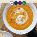 A bowl of carrot soupl on a wooden board with some bread