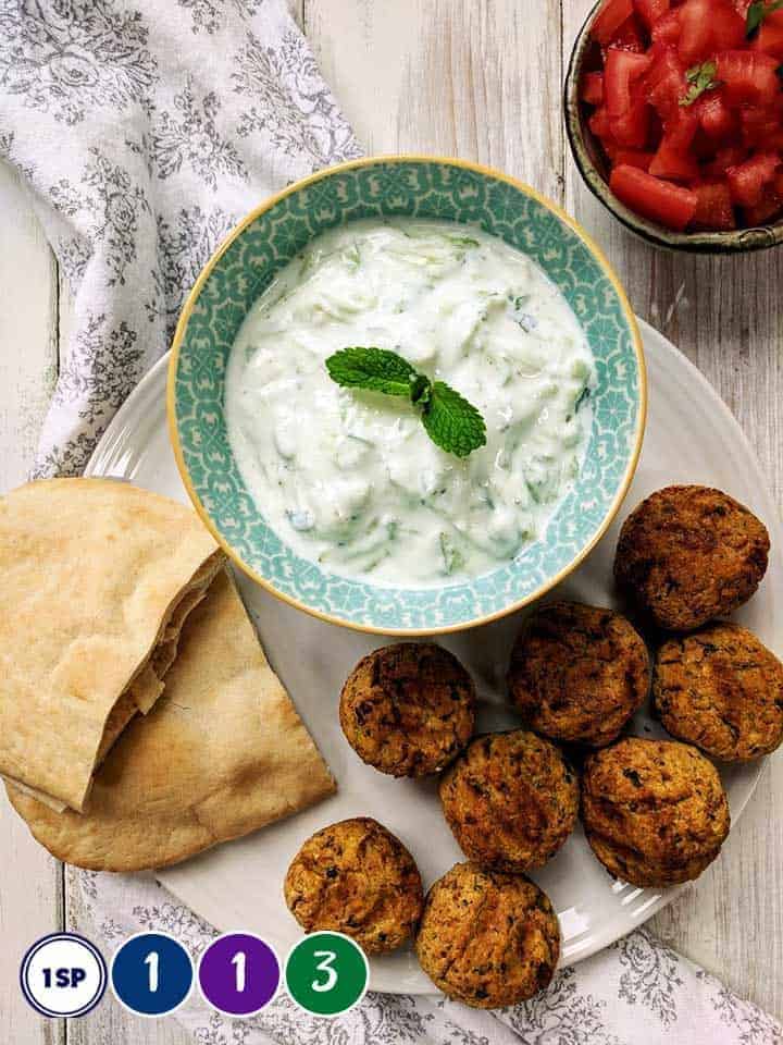 A white plate with falafel, pitta bread and tzatziki