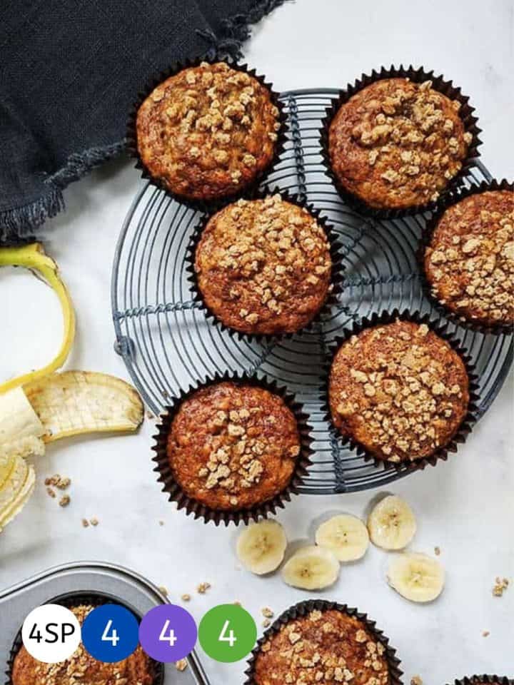 Six banana muffins on a wire rack cooling with banana slices beside them.