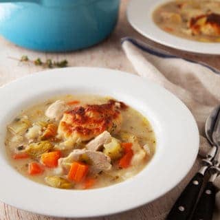 A white dish of chicken and dumplings on a wooden board