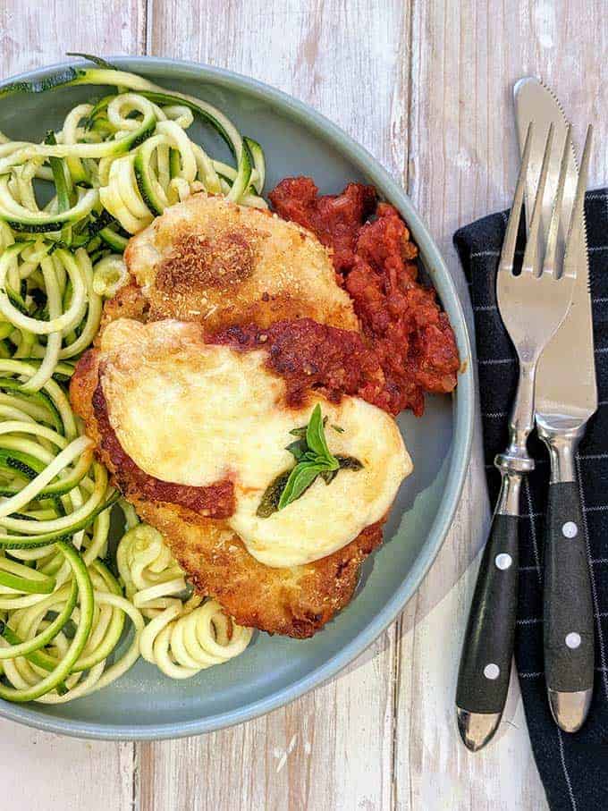 A plate of weight watchers chicken parmesan with zucchini noodles on a wooden table