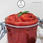 A jar of easy marinara sauce on a white table with some green basil