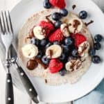 A berry breakfast taco on a white plate with black cutlery