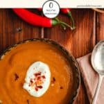 A bowl of curried pumpkin soup on a wooden table.