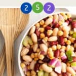 A bowl of three bean salad with a wooden serving spoon