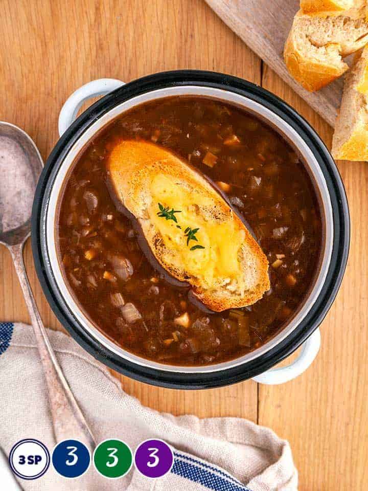 A bowl of French Onion Soup with a crouton on a wooden table