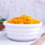A white dish on a white table full of squash mash