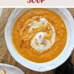 A bowl of carrot and lentil soup on a wooden table