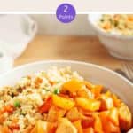 A white bowl of sweet & sour chicken with cauliflower rice on a wooden table