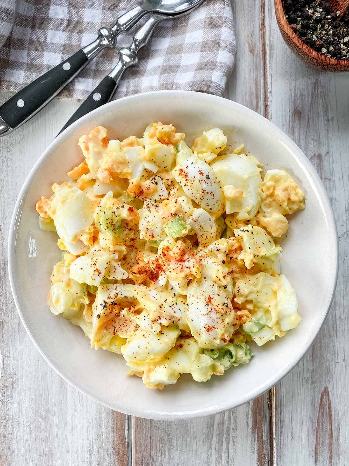 A white ceramic bowl full of egg salad on a wooden table