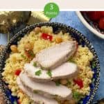 A decorative blue bowl full of couscous salad with sliced chicken on top
