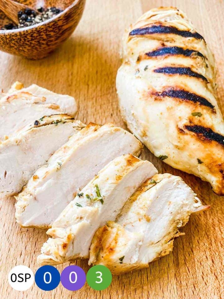 2 chicken breasts with grill marks on a wooden board.