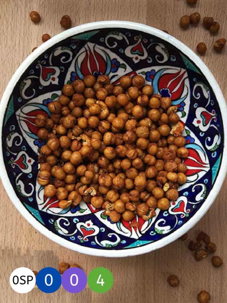 A red and blue painted bowl on a wooden table with roasted chickepeas.