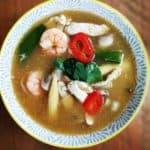 A ceramic bowl on a wooden table full of tum yum soup.
