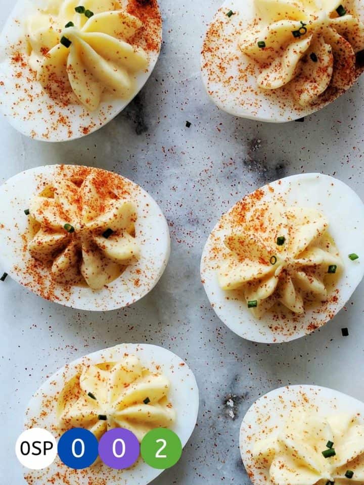 A marble table with 6 deviled eggs dusted with paprika and chives.