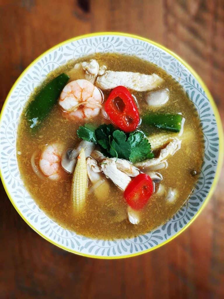 A bowl of tom yum soup on a wooden table.
