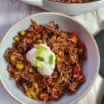A bowl of burrito mixture topped with yogurt and chopped spring onion on a white table.