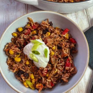 A bowl of burrito mixture topped with yogurt and chopped spring onion on a white table.