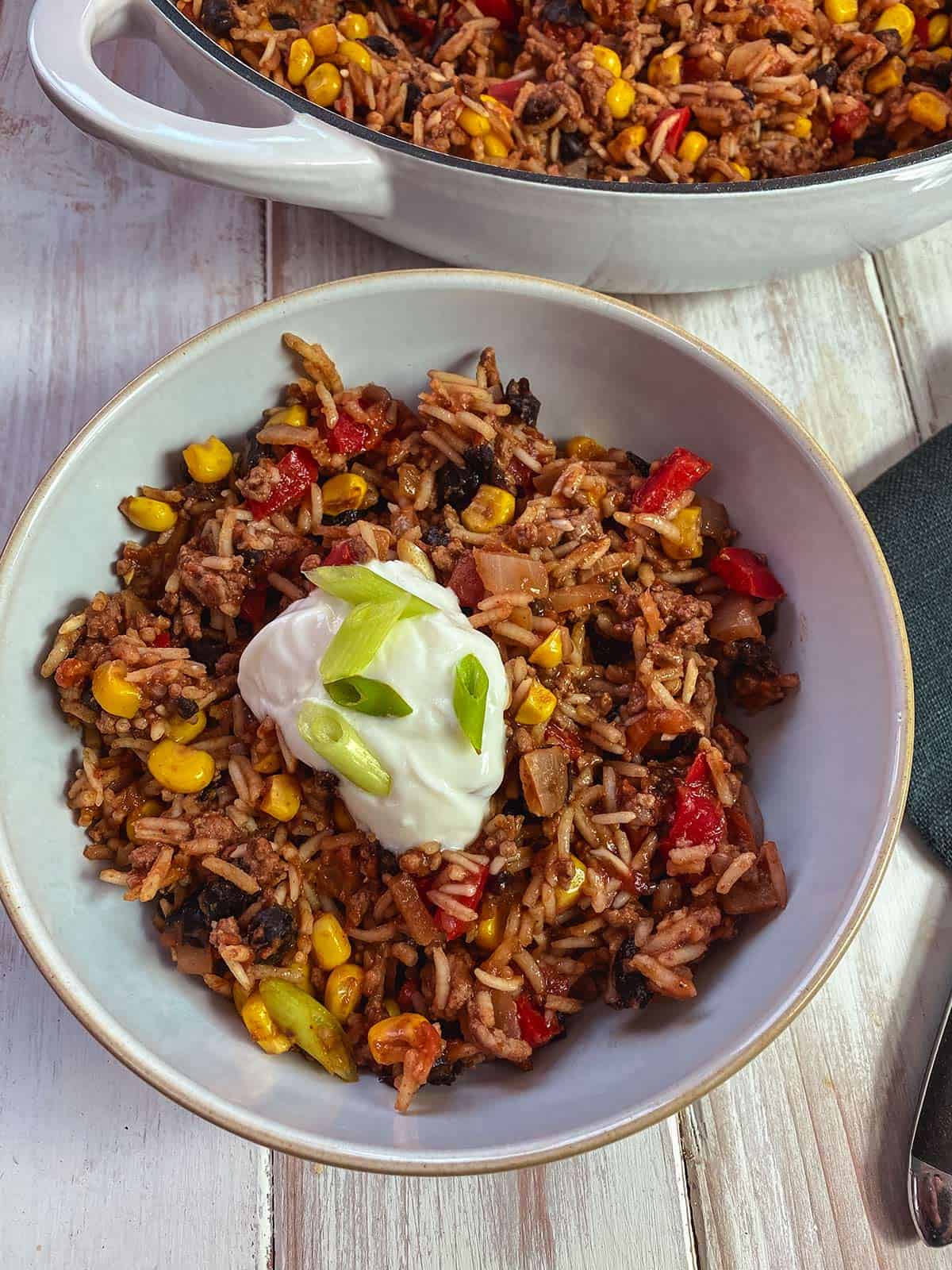 A bowl of burrito mixture topped with yogurt and chopped spring onion on a white table.