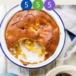 A dish of apple sponge pudding on a white table with a bowl of it with custard to the side.