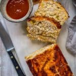 Sliced turkey meatloaf on a marble slab with a dish of tomato sauce on the side.