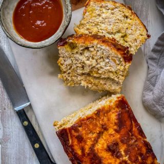 Sliced turkey meatloaf on a marble slab with a dish of tomato sauce on the side.