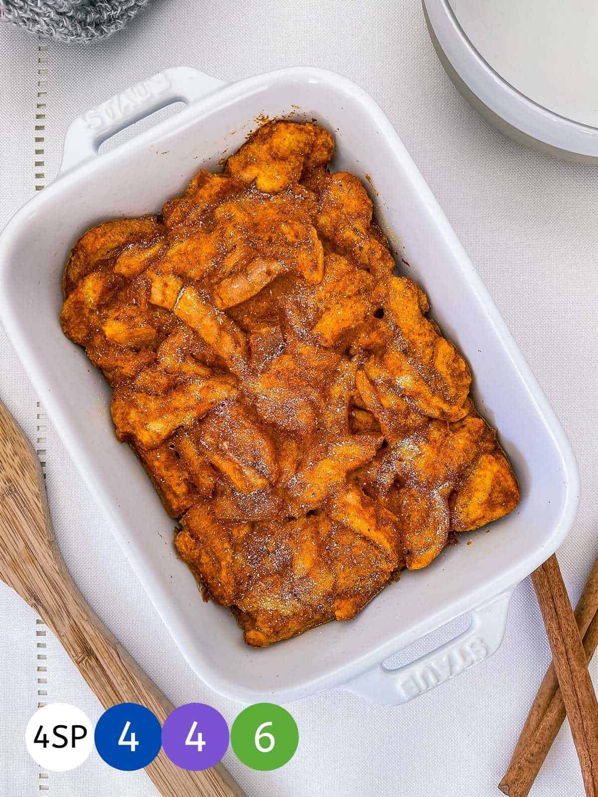 A dish of pumpkin french toast casserole on a white table with cinnamon sticks.
