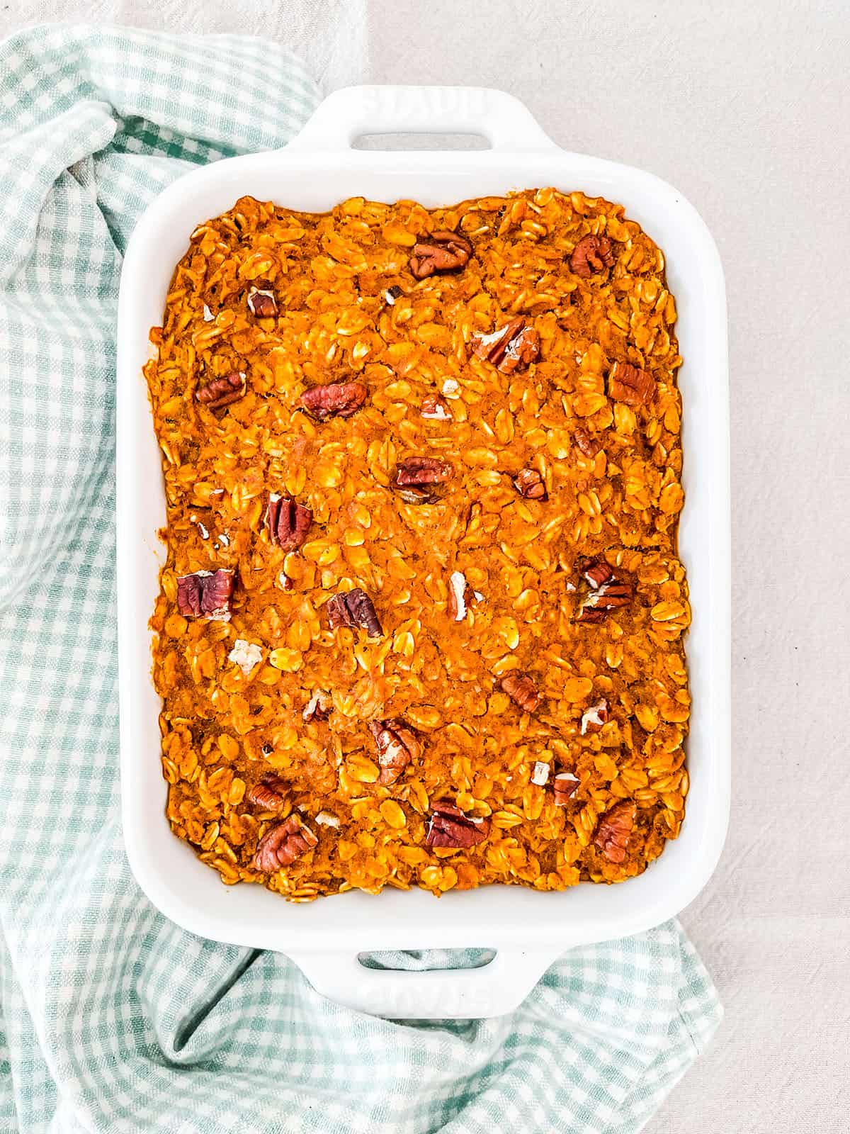 A dish of baked oatmeal topped with pecan nuts on a white table.