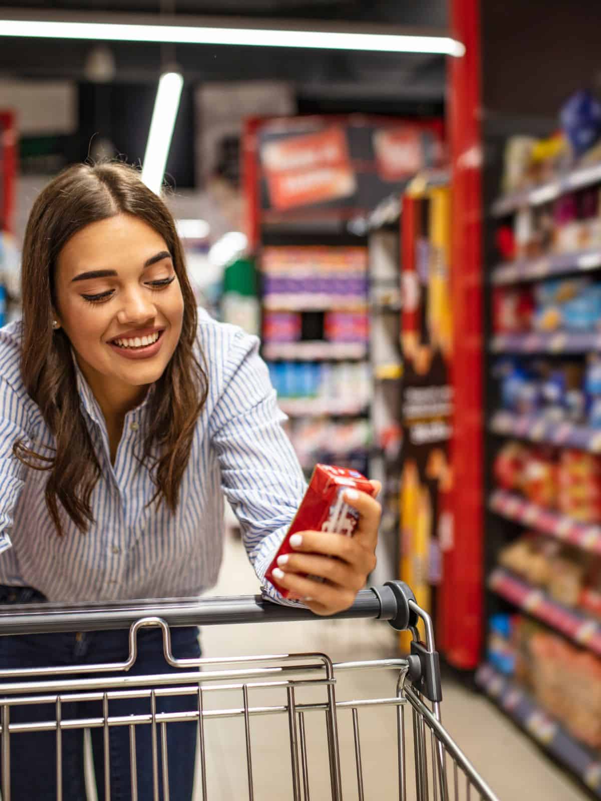 A woman looking at a carton whilst leaning on a shopping cart.